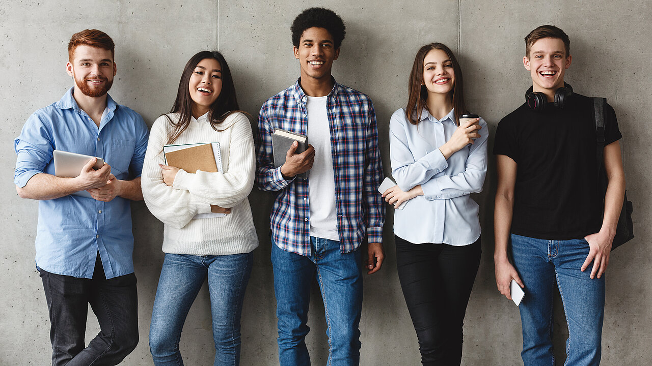 Eine Gruppe von jungen Frauen und Männern mit Büchern in der Hand lacht in die Kamera.