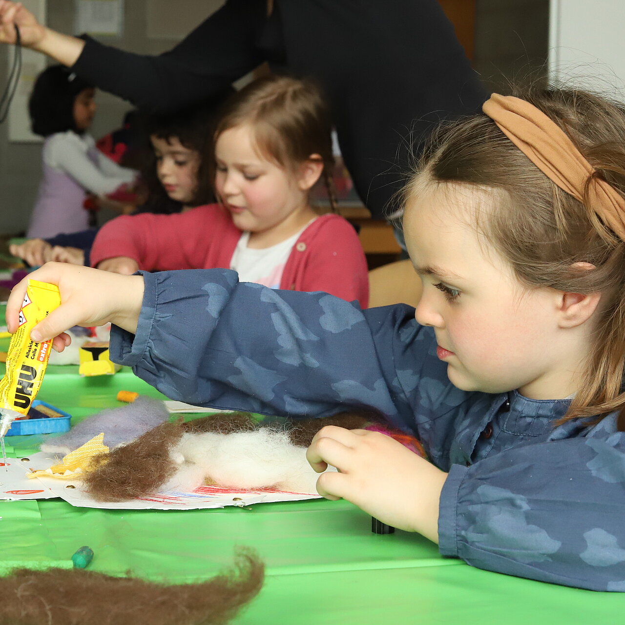 Kinder sitzen am Tisch und basteln mit Papier und Wolle.