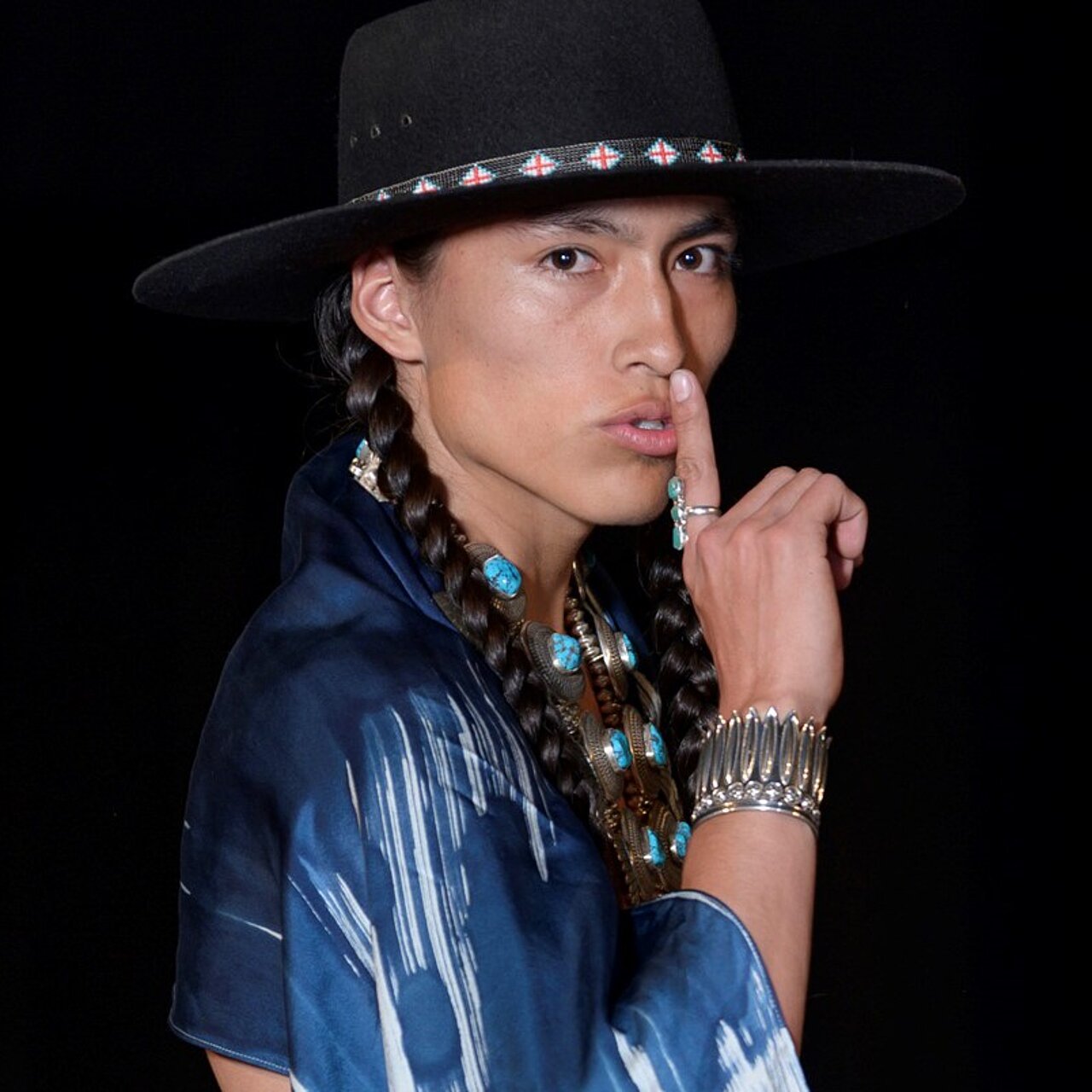 Ein indigener Mann mit Hut, geflochtenem Zopf und blauem Oberteil blickt in die Kamera.